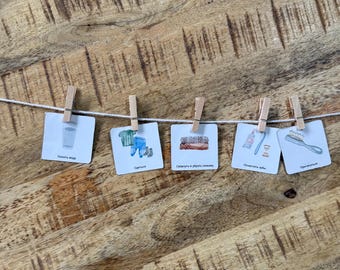 Puede incluir: Cinco tarjetas cuadradas blancas con ilustraciones y texto en ruso están sujetas a una cuerda blanca con pinzas de madera. Las tarjetas muestran un vaso de agua, ropa, ropa doblada, un cepillo de dientes con pasta y un cepillo para el pelo.