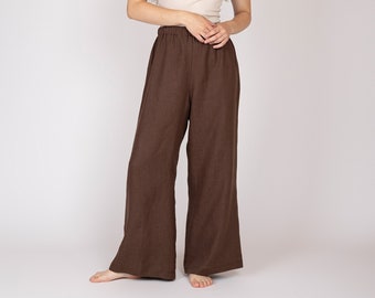 May include: A woman wearing a beige tank top and wide-leg brown pants. The pants have an elastic waistband. The outfit is simple and casual, suitable for everyday wear. The background is a plain white.