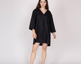 Pode incluir: Vestido preto com decote em V e mangas três quartos. O vestido tem uma silhueta solta e fluida e vai até meio da coxa. O tecido parece ser linho texturizado ou similar. Adequado para roupa casual.