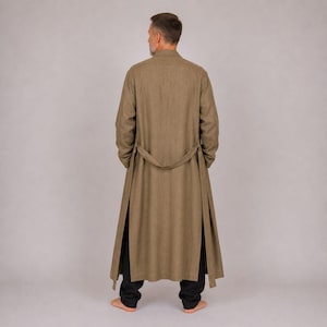 May include: A long, tan-colored coat with a matching belt, worn over black pants. The coat has a split design on the front, and the person is seen from the back.