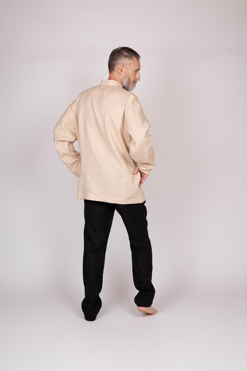 May include: A beige linen shirt with a mandarin collar and long sleeves, paired with black pants. The outfit is simple and classic, suitable for casual wear. The model is standing with their back to the camera.