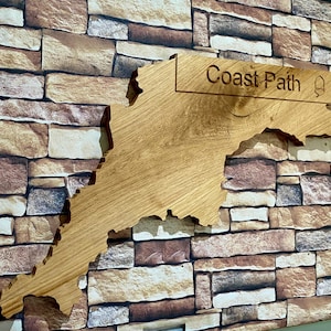 May include: A wooden sign shaped like a coastline with the words "Coast Path" carved into it. The sign is mounted on a brick wall.