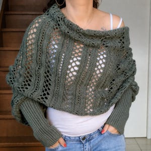 Peut inclure: Un boléro en crochet vert olive doté d'un corps large en maille lâche avec des rayures verticales texturées et des motifs ajourés. Le vêtement comprend de longues manches ajustées à poignets côtelés et une large encolure drapée tombante.