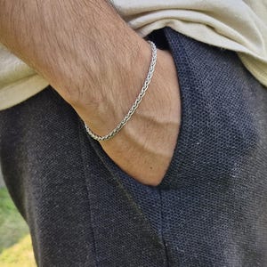 May include: A silver chain bracelet on a person's wrist. The bracelet is made of a braided chain design.