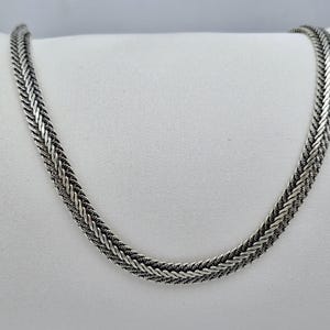 Puede incluir: Un collar de cadena de plata con un diseño trenzado.