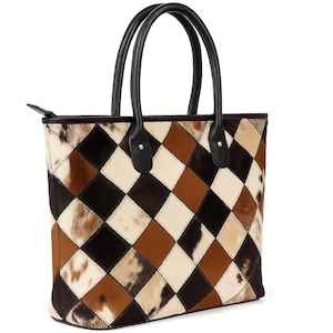 May include: A tote bag with a patchwork design in shades of brown, black, and cream. The bag features a diamond pattern and black leather handles. The bag has a zipper closure.