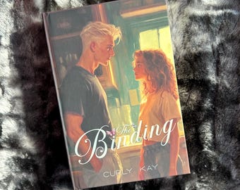 May include: The Binding by Curly Kay, a novel with a painted cover featuring a young man and woman looking at each other in a room with a window.