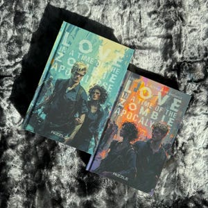 Puede incluir: Dos libros de bolsillo con portadas coloridas titulados "Love in a Time of the Zombie Apocalypse". El primer libro tiene una portada azul, amarilla y roja con un hombre y una mujer en la portada. El segundo libro tiene una portada roja, naranja y amarilla con tres personas en la portada.