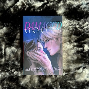 May include: A book cover with a pink and blue gradient title "DAMAGED GOODS" and the subtitle "SLYTHERIN AFTER DARK". The cover features a close-up of two people, a woman with dark hair and a man with light hair, looking at each other.