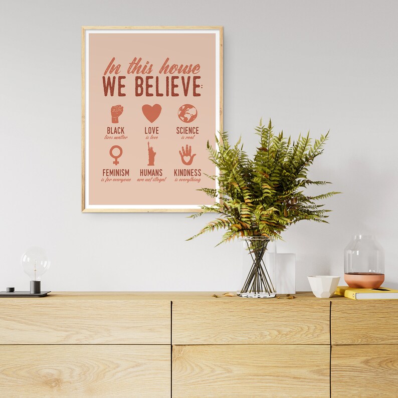 Pu&ograve; includere: Un poster rosa e marrone con il testo "In questa casa crediamo:" e un elenco di valori che includono "Le vite nere contano", "L'amore &egrave; amore", "La scienza &egrave; reale", "Il femminismo &egrave; per tutti", "Gli umani non sono illegali" e "La gentilezza &egrave; tutto".
