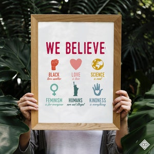 May include: A framed poster with the text "WE BELIEVE" in red letters. The poster features a series of illustrations and text, including "BLACK lives matter", "LOVE is love", "SCIENCE is real", "FEMINISM is for everyone", "HUMANS are not illegal", and "KINDNESS is everything".