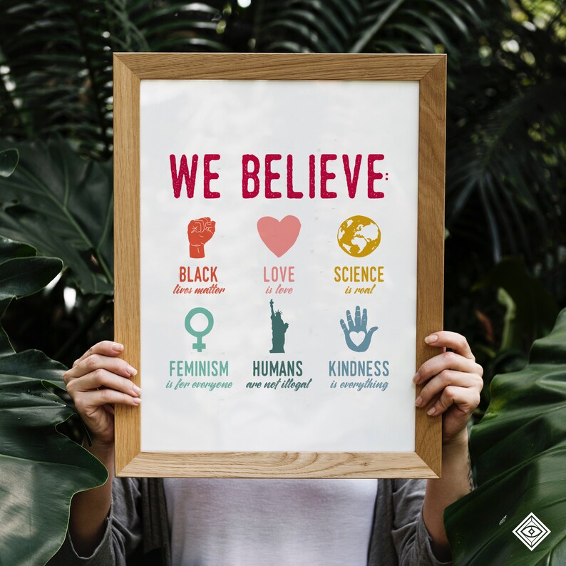 May include: A framed poster with the text "WE BELIEVE" in red letters. The poster features a series of illustrations and text, including "BLACK lives matter", "LOVE is love", "SCIENCE is real", "FEMINISM is for everyone", "HUMANS are not illegal", and "KINDNESS is everything".