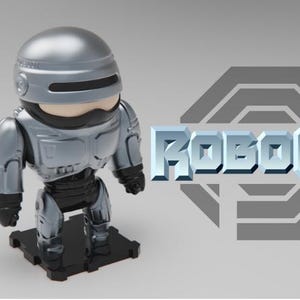 May include: A silver and black Robocop figurine with the word "ROBOCOP" in silver block letters. The figurine is on a black base, with a speech bubble containing the numbers "120".