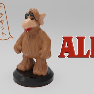 May include: A brown furry figure with large ears and a red nose stands on a black base. The figure is a toy of the alien character ALF from the 1980s television show. The text "ALF" is written in red letters in the background. The text "プラキット" is written in Japanese in a speech bubble above the figure.