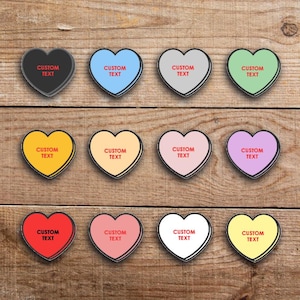 May include: A collection of twelve heart-shaped objects in various colors, each with a white border and the words "CUSTOM TEXT" in red. The hearts are arranged on a wooden surface, offering a customizable design.