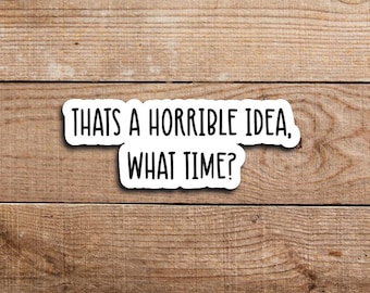 May include: A white sticker with black text that reads "THAT'S A HORRIBLE IDEA, WHAT TIME?" The sticker is rectangular with rounded corners and is set against a wooden background.