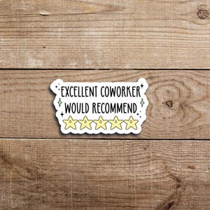 May include: A white sticker with the text "EXCELLENT COWORKER WOULD RECOMMEND" in black, with five yellow star ratings. The sticker has a decorative border and is set against a wooden background.