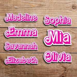 May include: Pink and white name stickers on a wooden surface. The stickers feature the names Madeline, Sophia, Emma, Mia, Savannah, Elizabeth, and Olivia in a decorative font.