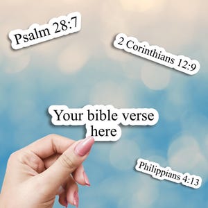 May include: White stickers with black text featuring Bible verses: Psalm 28:7, 2 Corinthians 12:9, Philippians 4:13, and "Your bible verse here". The stickers are on a blue and white blurred background.
