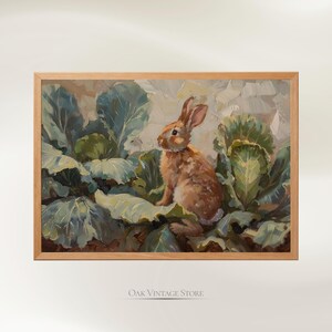 May include: A framed painting depicts a brown rabbit nestled among large green cabbage leaves. The artwork has a vintage aesthetic, with a light brown wooden frame. The painting's style is reminiscent of classic oil paintings.