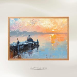 Può includere: Stampa di pittura a olio incorniciata. L'opera raffigura una persona seduta su un molo di legno, che si affaccia su un lago calmo al tramonto. Il cielo è pieno di vibranti tonalità arancioni, rosa e gialle, che si riflettono sull'acqua.