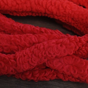May include: Bright red, textured fabric in a looped design. The material is arranged in a loose, intertwined pattern, creating a soft, inviting appearance. The color is a vibrant, solid red, suitable for various craft projects.
