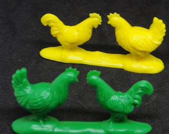 May include: Four plastic toy chickens, two yellow and two green, standing on bases of the same color. The chickens are facing each other in pairs.
