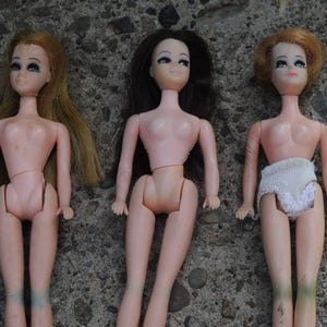 May include: Three vintage fashion dolls with rooted hair in blonde, brown, and auburn. The dolls are nude, with articulated limbs and painted facial features. The text "sold separately" is visible.
