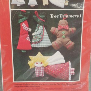 May include: A package for a patchwork pattern and instructions by Yours Truly. The cover features illustrations of handmade Christmas tree ornaments, including angels, gingerbread people, and figures in dresses and hats. The text reads "Tree Trimmers 1".