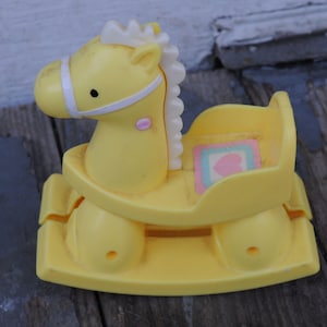 May include: A yellow plastic toy rocking horse with a white mane and bridle. The horse has a seat with a small, colourful design. The toy is designed for young children and is made of durable plastic.