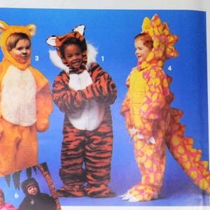May include: Three children wearing animal costumes. A child in a yellow and pink dinosaur costume, a child in a tiger costume, and a child in a yellow and white tiger costume.