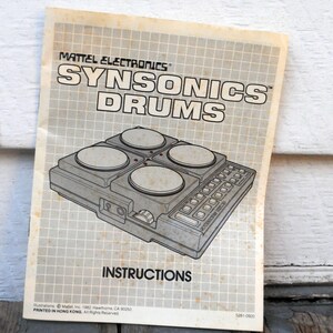 May include: A black and white illustration of a vintage electronic drum set with four pads and a control panel. The text "MATTEL ELECTRONICS SYNSONICS DRUMS" is printed in bold at the top of the image. The text "INSTRUCTIONS" is printed in bold at the bottom of the image.