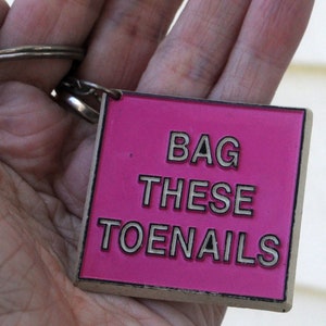 May include: Pink keyring with the text "BAG THESE TOENAILS" in white lettering.
