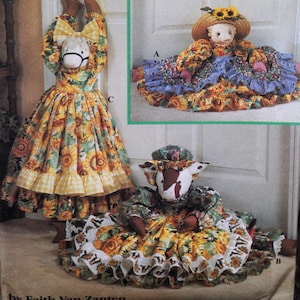 May include: Three handmade fabric dolls with animal heads and floral dresses. One doll is a horse, another a cow, and the third has a doll face. The dresses feature sunflower and gingham patterns. The image is labeled "by Faith Van Zanten."
