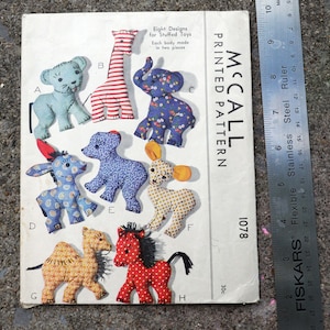 May include: Vintage McCall's printed pattern for stuffed toys. The pattern features eight different animal designs, including a giraffe, elephant, and horse. The pattern is printed on a white paper with the text "McCall Printed Pattern 1078".
