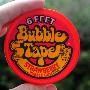 May include: Red and yellow bubble gum tape container with the text "6 Feet of Bubble Tape" and "Strawberry Bubble Gum Artificial Flavor". The container has a net weight of 60 g (2.10 oz).