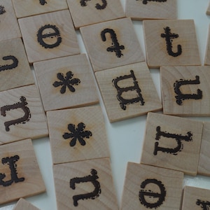 May include: Wooden letter tiles with dark brown, burnt-in letters and symbols. The tiles are square and made of light-colored wood. The letters include h, e, t, u, y, n, j, and m, along with asterisks.