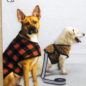 May include: Two dogs wearing winter coats. The dog on the left is wearing a red and black plaid coat. The dog on the right is wearing a brown and black coat. Both dogs are wearing leashes.