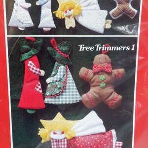 May include: A collection of handmade Christmas tree ornaments. The image features various fabric ornaments, including angels, gingerbread people, and figures in dresses and hats. The text "Tree Trimmers 1" is visible.