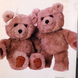 May include: Two brown teddy bears, one with a pink bow, sitting side by side. The bears have brown fur and black eyes.