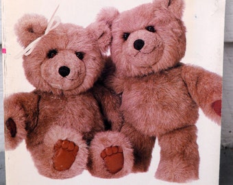 May include: Two brown teddy bears, one with a pink bow, sitting side by side. The bears have brown fur and black eyes.