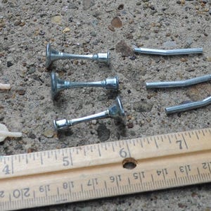 May include: A collection of miniature game pieces including three silver-colored pistols, three beige rope loops, three silver-colored candlesticks, three silver-colored pipes, three silver-colored daggers, three silver-colored wrenches, and a white die.