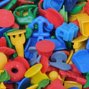May include: A colorful assortment of small plastic toys in various shapes, including boats, anchors, and circles. The toys are primarily red, blue, yellow, and green, creating a vibrant and playful mix. These toys are likely for children's games or educational activities.