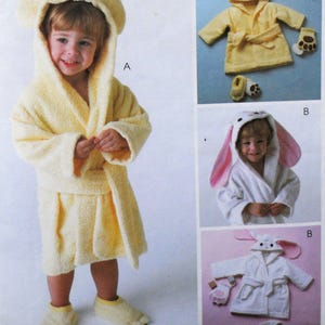 May include: A child wearing a yellow terry cloth bathrobe with a hood featuring bear ears. The robe has a matching belt and is paired with bear paw slippers. The image also shows a similar robe with bunny ears.