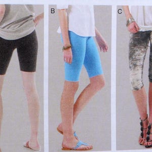 May include: Three pairs of women's shorts are shown. The first is black, the second is light blue, and the third features a patterned design in grey and white. The shorts are knee-length and appear to be made of a stretchy material.