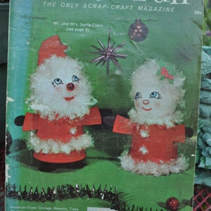 Peut inclure: Une couverture de magazine Pack-O-Fun de décembre 1973. Elle présente des figurines du Père Noël faites à la main, vêtues de rouge et de blanc, sur fond vert. Le magazine promeut des projets d'artisanat.