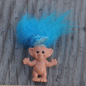 Könnte beinhalten: Eine kleine blaue Trollpuppe mit einem blauen und weißen Stirnband. Der Troll hat einen hellbraunen Körper und ein breites Lächeln.