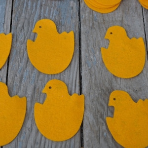 May include: Nine yellow felt chick shapes with a beak and eye detail. The chicks are arranged in a row on a wooden surface.