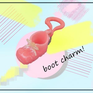 May include: A pink boot charm with a loop handle and a small bow detail. The charm is set against a pastel background with the text "boot charm!"
