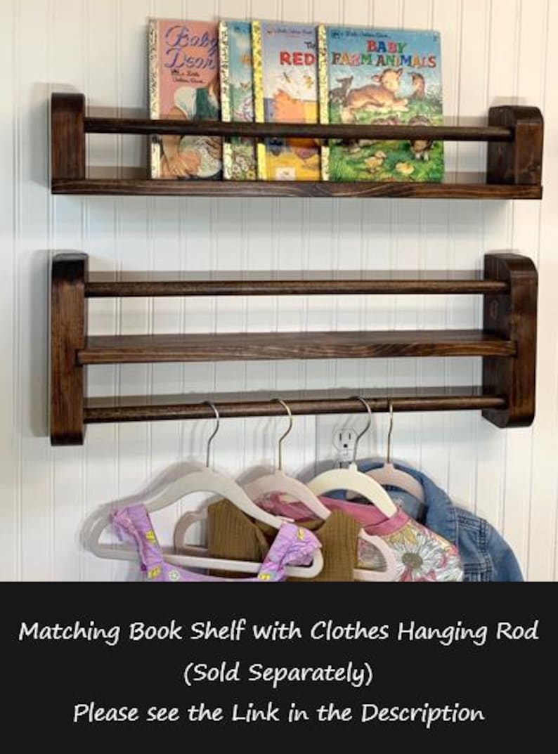 May include: Dark brown wooden wall-mounted bookshelf with two shelves. The top shelf holds vintage children's books. Below, a clothes hanging rod holds several children's garments. The text in the image says "Matching Book Shelf with Clothes Hanging Rod (Sold Separately)"